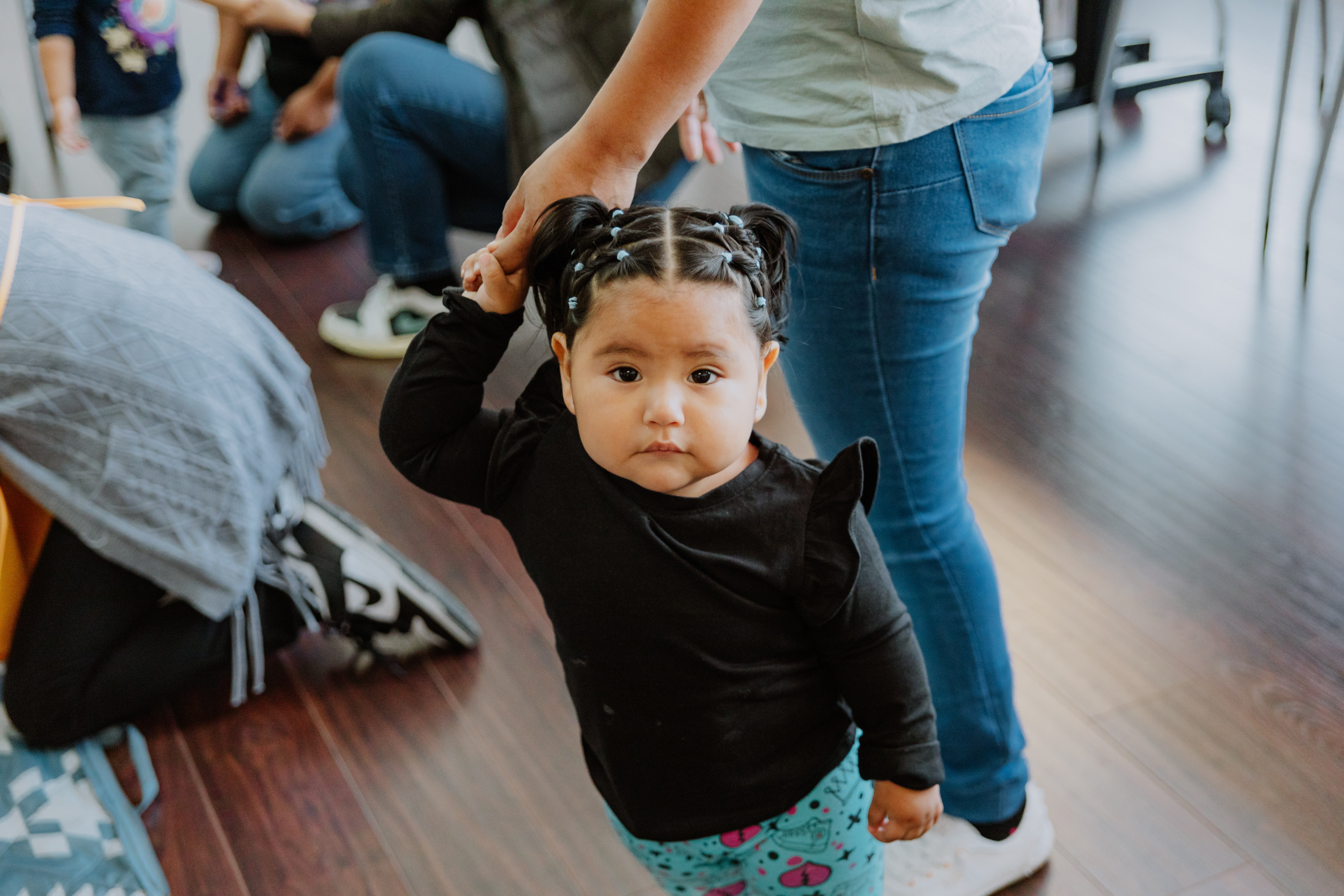 Young child holding caregiver's hand and looking up at camera.