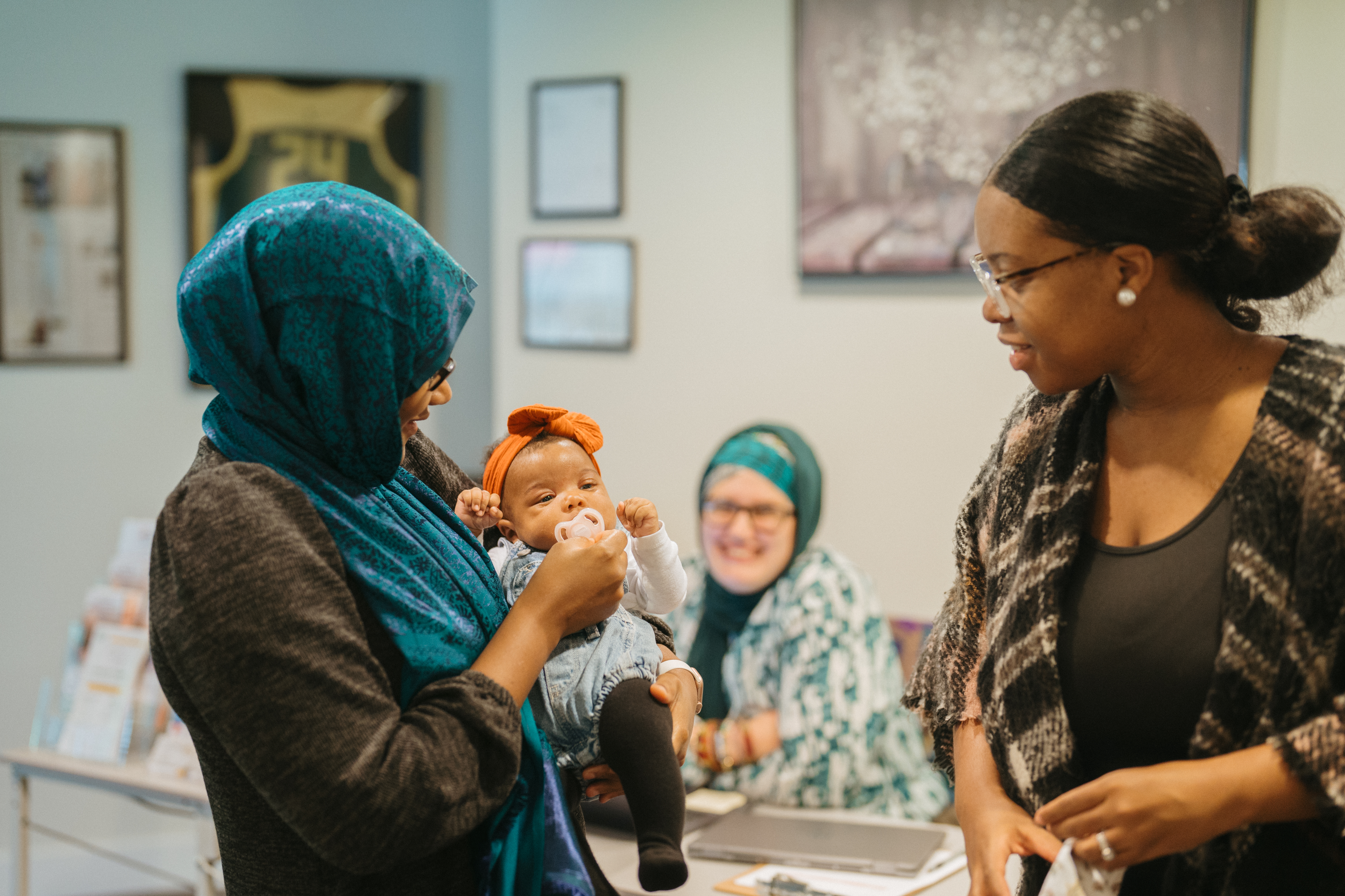 Caregiver holding a baby with other adults smiling and observing.
