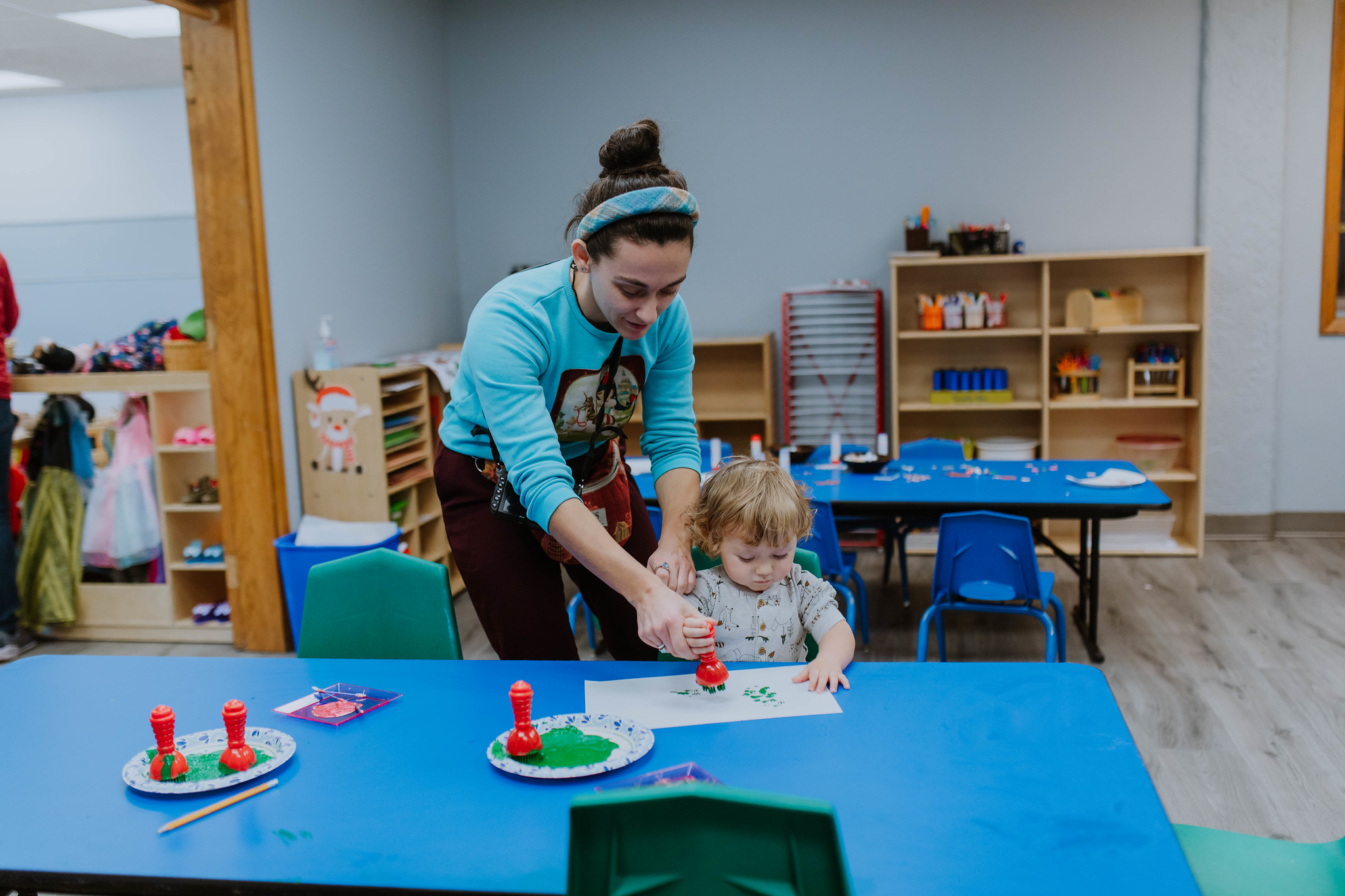 Image of child care type setting : an adult helping a young child with an art project.