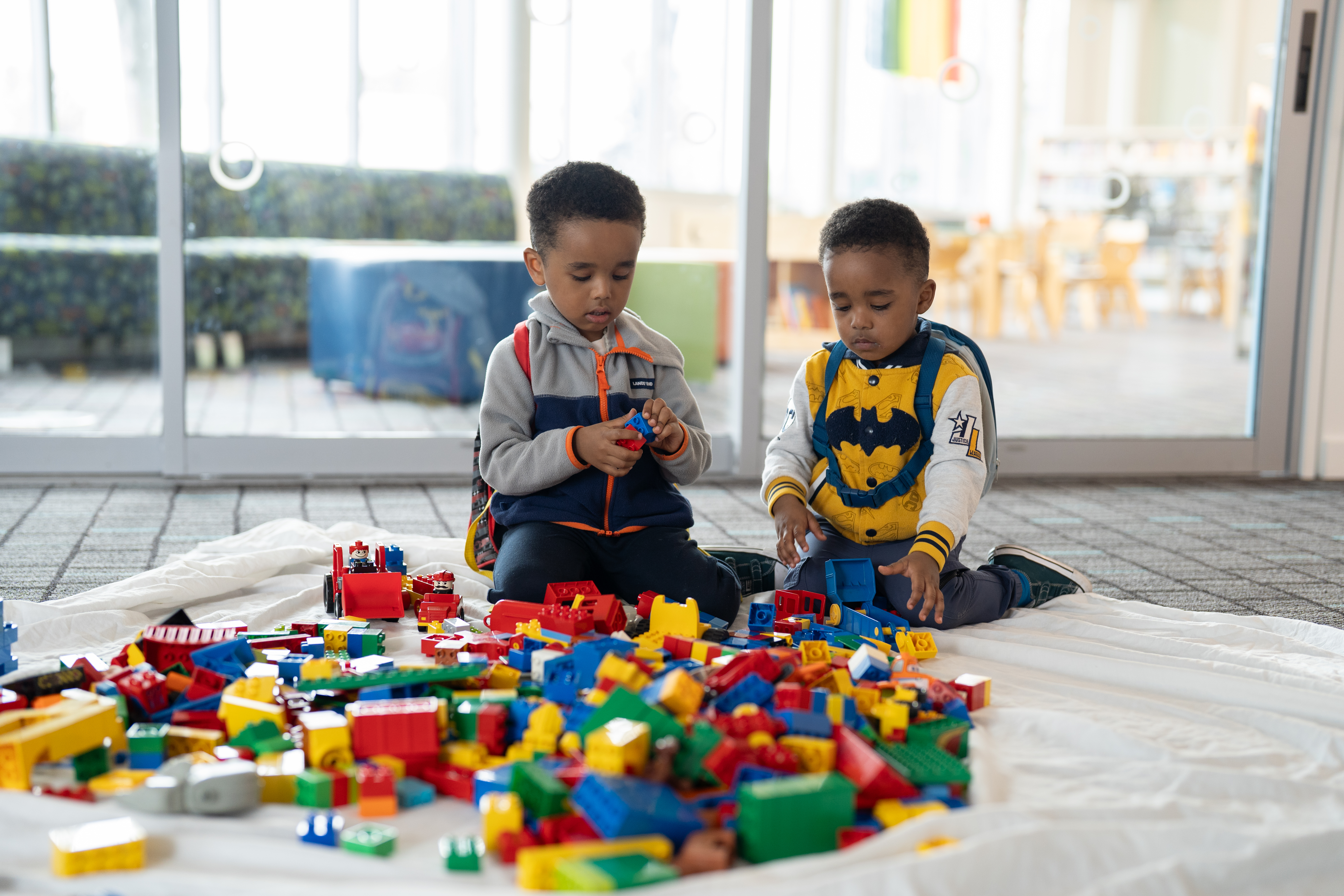 Two young black boys sitting on the ground playing with legos.