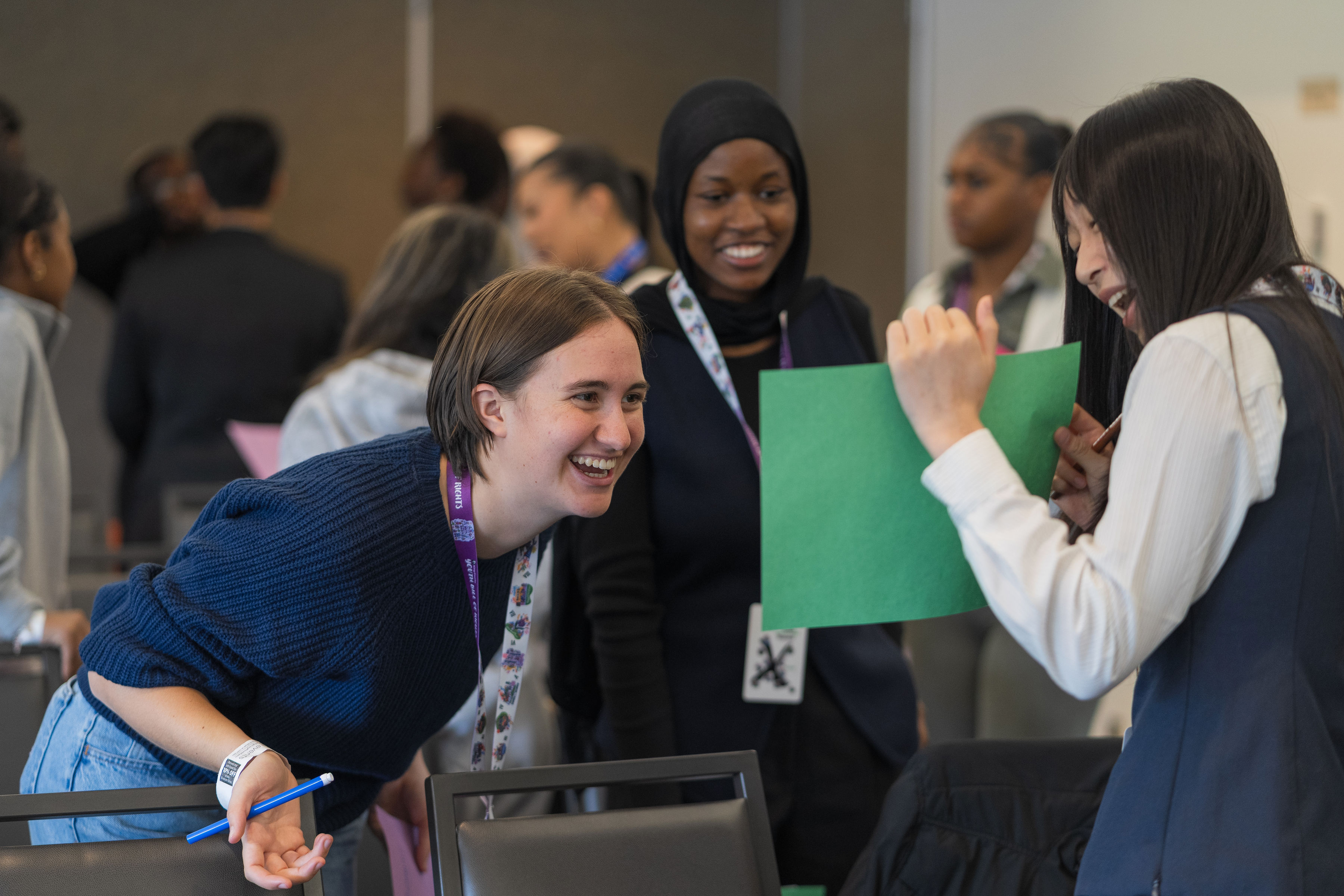 Three young people of varying skin tones joyfully conferring at the Youth Leadership Summit.