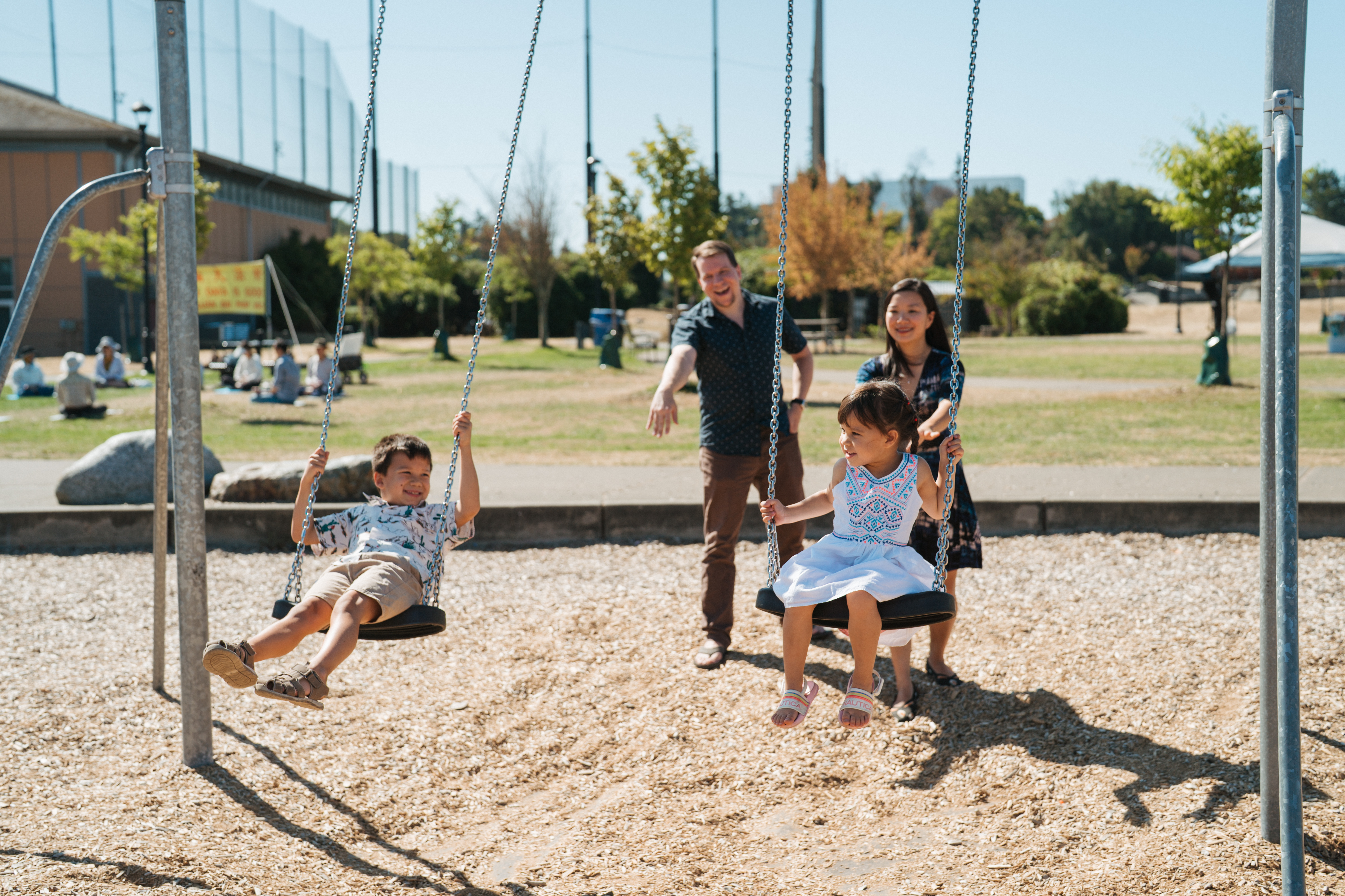 Parents pushing young kids on outdoor swing set