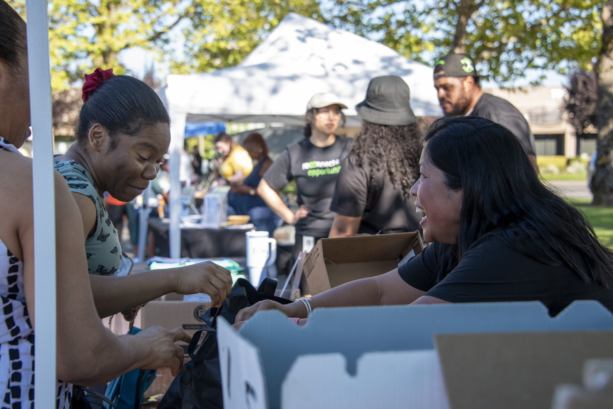 ReConnect to Opportunity staff member, smiling, hands resources to a community member, also smiling.
