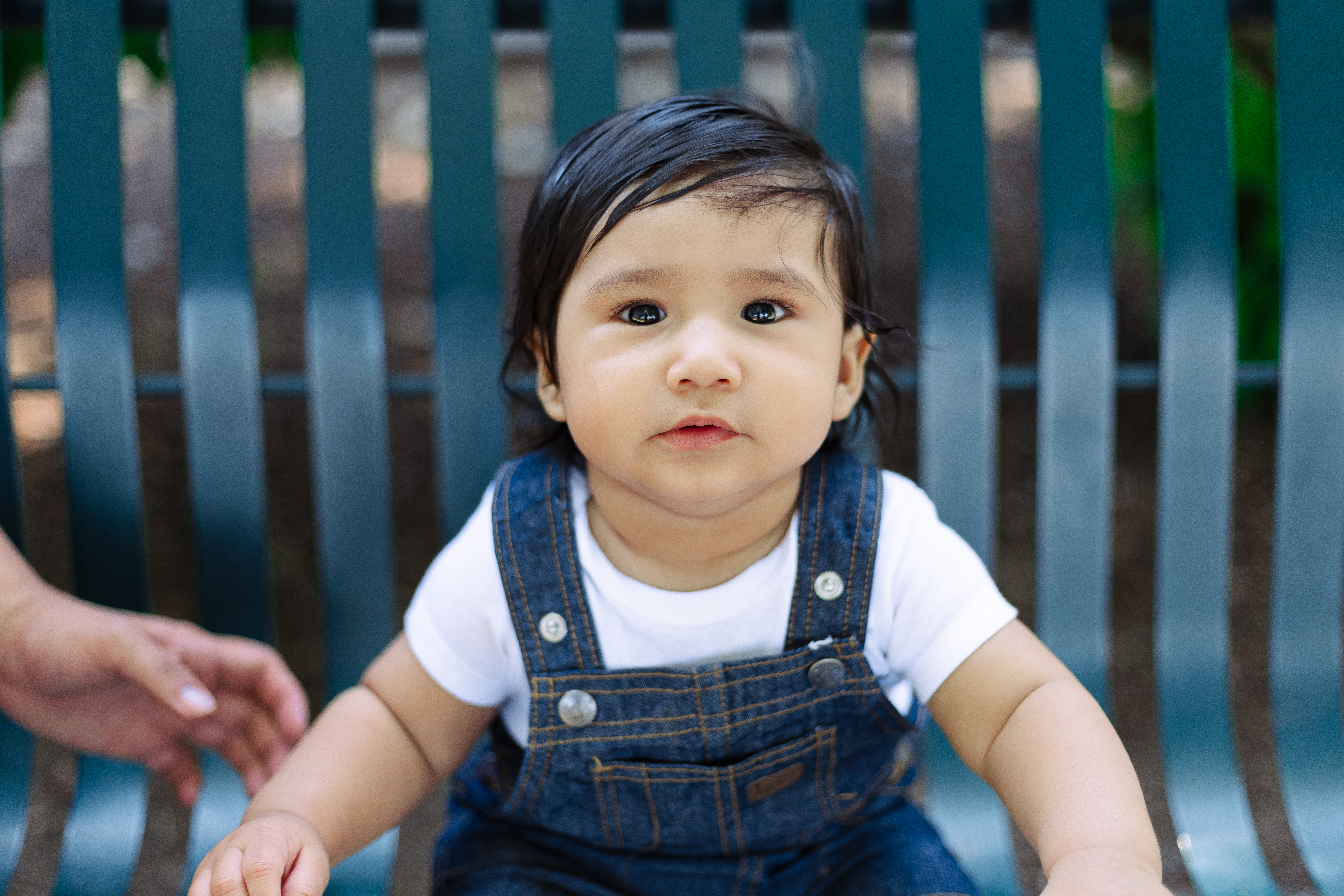 Young child sitting on bench looking up at camera.